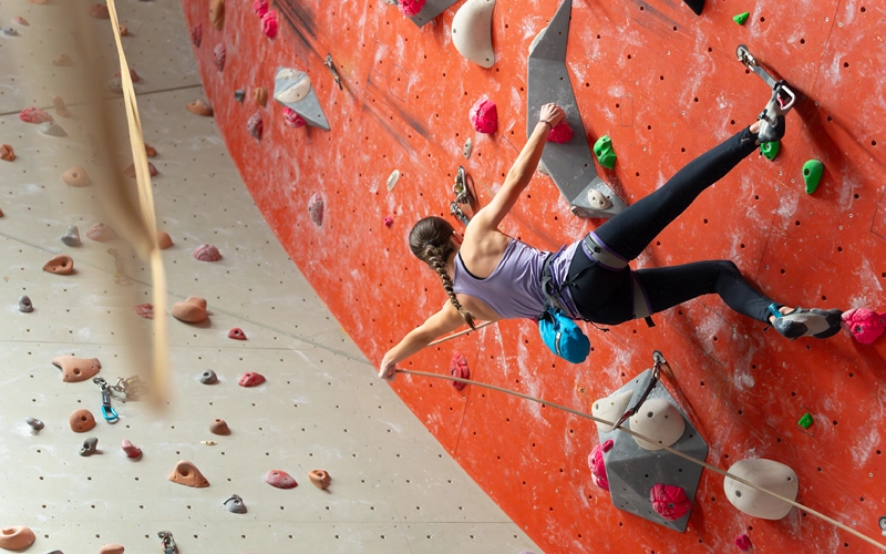 Climber stretching across an orange indoor climbing wall