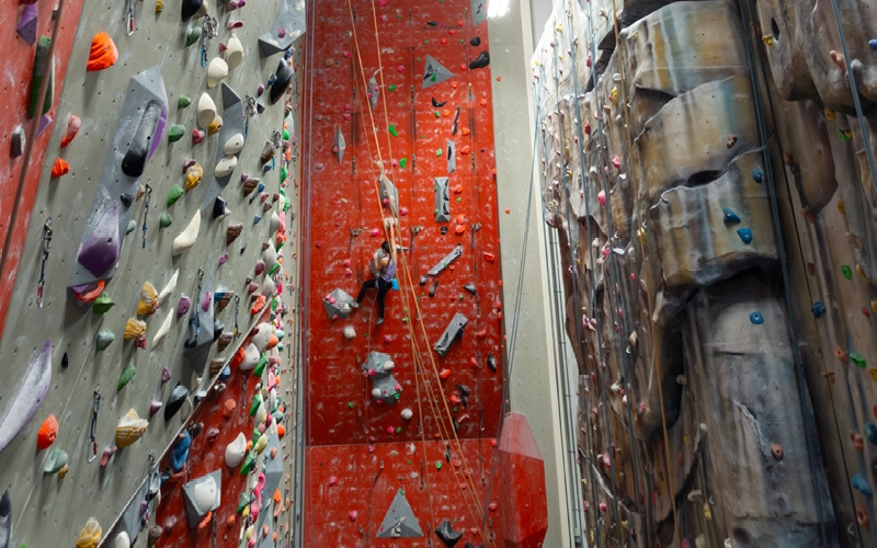 A climber looking up at routes on a tall indoor climbing wall